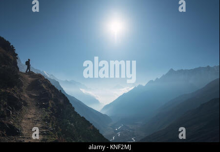 Jeune femme debout sur la colline et à la vallée de montagne. Paysage avec girl, chemin, montagne, ciel bleu avec soleil et nuages bas au lever du soleil dans N Banque D'Images