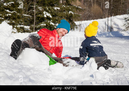 Homme et Fils rire après la chute de toboggan dans snow covered landscape Banque D'Images