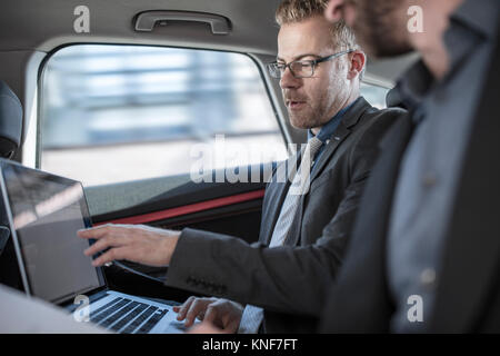 Deux hommes assis à l'arrière de la voiture, regardant un écran d'ordinateur portable Banque D'Images