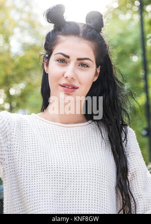 Portrait de jeune femme élégante avec de longs cheveux noirs et cheveux buns in city park Banque D'Images