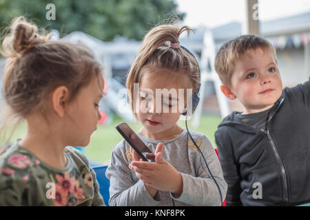 Jeune fille avec des amis, à l'aide de smartphone, portant des écouteurs Banque D'Images