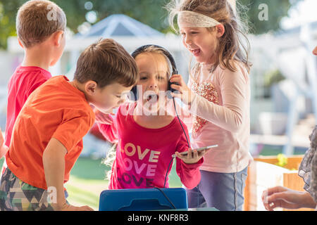 Jeune fille avec des amis, holding smartphone, portant des écouteurs Banque D'Images