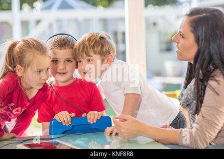 Mid adult woman sitting avec trois jeunes enfants, jeune garçon holding digital tablet, portant des écouteurs Banque D'Images