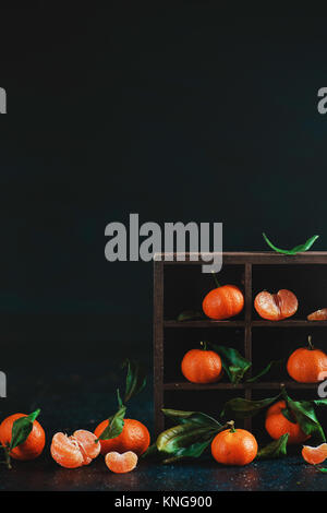 Mandarines dans une boîte en bois sur un fond sombre. La photographie alimentaire sombre avec des fruits orange vif et copiez l'espace. Banque D'Images