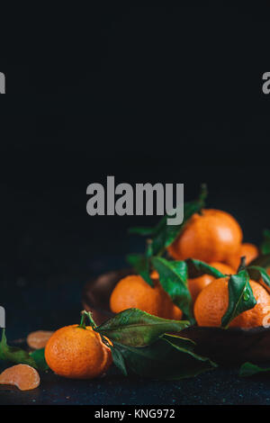 Agrumes sur une plaque de bois avec des feuilles vertes. Tangerines dynamique sur un fond sombre. La photographie culinaire rustique. Banque D'Images