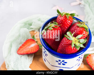 Une fraise mûre en émail mug sur planche de bois avec le textile. Printemps Été collation santé aux fruits Banque D'Images