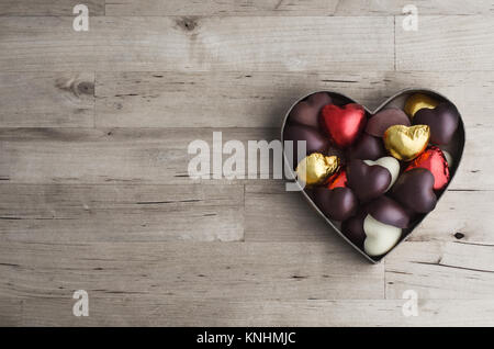 Coup de tête en forme de coeur ouvert boîte contenant une variété de chocolats faits maison sur les vieux, usé la planche en bois clair table. Banque D'Images