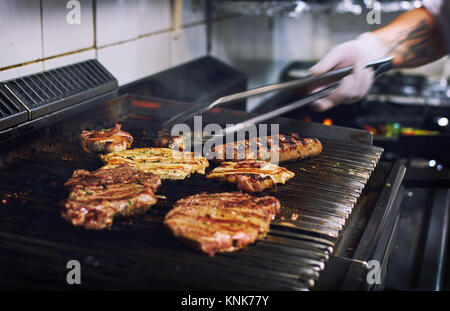 Chef mains cuisine viande assortis sur la grille du barbecue dans la cuisine du restaurant Banque D'Images