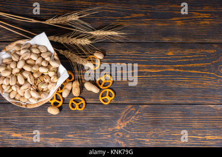 Vue du dessus de la plaque en bois avec les pistaches, près de blé, les bretzels et petits dispersés arachides sur vieux dark 24. Aliments et boissons concept Banque D'Images