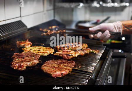 Chef mains cuisine viande assortis sur la grille du barbecue dans la cuisine du restaurant Banque D'Images