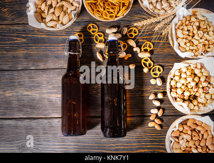 Vue de dessus de la bière différentes collations dans les assiettes comme les pistaches, les petits bretzels et arachides, près de deux des bouteilles de bière en bois foncé 24. Aliments et boissons co Banque D'Images