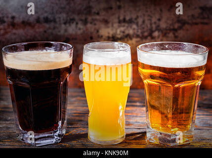 Trois verres de lumière, non filtré et bière brune sur un bureau en bois sombre. Aliments et boissons concept Banque D'Images