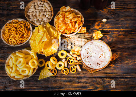 Vue de dessus des plaques avec des collations près de verre de bière, de blé, d'écrous et les bretzels dispersés sur un bureau en bois sombre. Aliments et boissons concept Banque D'Images