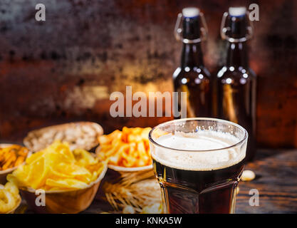 Les plaques avec des collations près de deux bouteilles et un verre de bière brune, blé, noix et dispersés sur les bretzels en bois 24. Aliments et boissons concept Banque D'Images