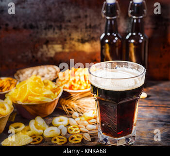 Les plaques avec des collations près de deux bouteilles et un verre de bière brune fraîchement coulé, blé, noix et dispersés sur les bretzels en bois 24. Restauration et Boissons Banque D'Images