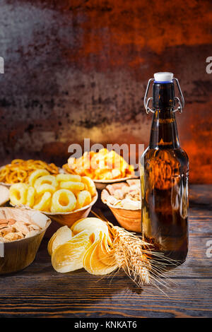 Bouteille de bière près de plaques avec les pistaches, noix et autres en-cas savoureux, blé et dispersés sur des jetons en bois 24. Aliments et boissons concept Banque D'Images