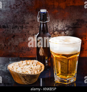 Verre à bière légère fraîchement coulé, bouteille de bière près de plaque de bois avec les pistaches sur une surface miroir noir. Aliments et boissons concept Banque D'Images