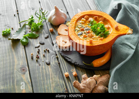 Soupe de potiron épicée assaisonné de gingembre, le piment et l'ail, servi dans une citrouille évidée avec croûtons, persil et graines de citrouille. Les aliments d'automne backgrou Banque D'Images