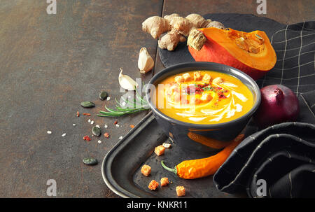Soupe de potiron épicée au gingembre et l'oignon, servie dans un bol avec l'huile de citrouille noir, crème fraîche, graines de citrouille et le persil sur la table en bois. C'est l'allemand Banque D'Images
