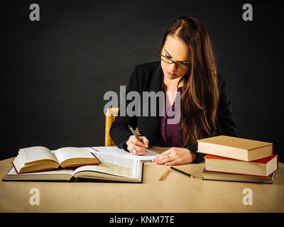 Photo d'un enseignant ou d'affaires femme d'une 30 ans assis à un bureau devant un grand tableau noir par écrit. Banque D'Images