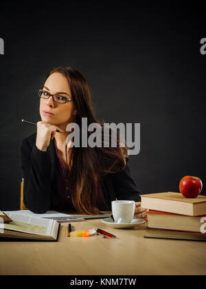 Photo d'un enseignant ou d'affaires femme d'une 30 ans assis à un bureau devant un grand tableau noir. Banque D'Images