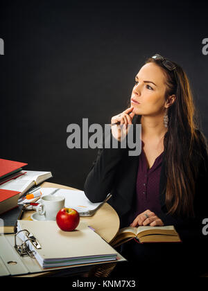 Photo d'un enseignant de ses 30 ans assis à un bureau malpropre devant un grand tableau noir en lisant un livre. Banque D'Images