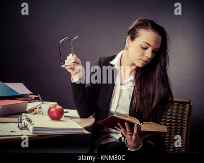Photo d'un enseignant de ses 30 ans assis à un bureau malpropre devant un grand tableau noir en lisant un livre. Banque D'Images