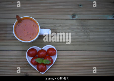 La photographie alimentaire droit d'accueil et tomate soupe aux herbes dans une tasse d'amour plat en forme de coeur rempli de légumes frais et basilic sur bois rustique Banque D'Images