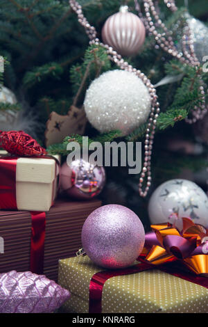 Une pile de boîtes-cadeaux de taille différente avec des rubans sous un arbre de Noël décoré. Blanc, rose et violet balles faites de verre et de perles brillantes sur fi Banque D'Images