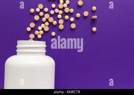 Groupe d'autres comprimés beiges. Capsules spilling out of white bouteille. Fond violet. Banque D'Images