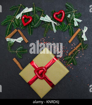 Une fête lumineuse composition d'une boîte-cadeau attaché avec du ruban métallique rouge, branches d'épinette, de paillettes, de coeur et des bâtons de cannelle dans une forme de cœur. D Banque D'Images