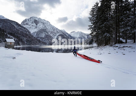 Homme portant un kayak rouge sur une froide journée d'hiver au lac de Predil d'avoir certaines activités récréatives d'hiver dans la neige, les Alpes, l'Italie. Banque D'Images