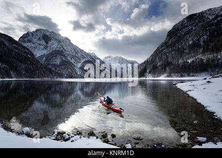 Homme dans un kayak rouge faisant les loisirs d'hiver sur une froide journée d'hiver au lac de Predil dans la neige, les Alpes, l'Italie. Banque D'Images