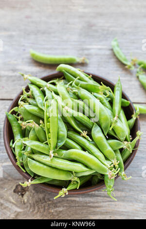 Les jeunes pois dans une plaque d'argile sur une table en bois. debout à côté d'une assiette de gousses de pois. à côté de la plaques est la tige de pois. Banque D'Images