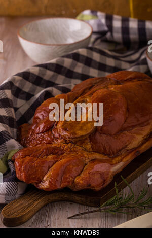 Photo verticale avec de gros morceau de viande de porc fumé avec de l'os placé sur une planche à découper. Serviette bleu, broyeur, fourchette, bols et romarin sont autour avec win Banque D'Images