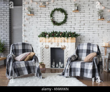 Fête de Noël à l'intérieur couleurs gris et blanc. Couronne verte ronde blanc accroché sur mur de briques. Deux fauteuils recouverts de couvertures douillettes debout Banque D'Images