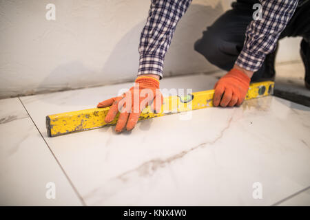 Accueil tile amélioration - handyman avec niveau fixant plancher de tuiles Banque D'Images