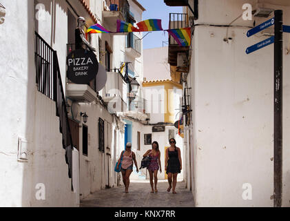 Trois jeunes femmes à pied dans gay street d'Ibiza en plein jour. Rue étroite et blanc, traditionnel bâtiments reflètent le style de vie de l'île et de la culture. C'est Banque D'Images