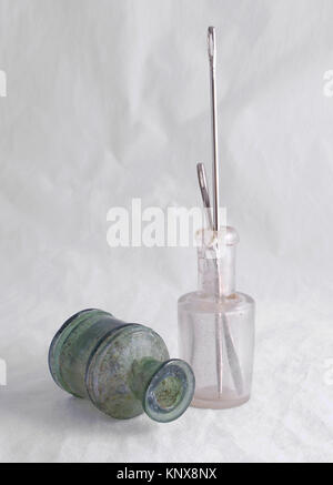 Deux anciennes petites bulles, vert et transparent, couleur sur fond blanc, dans une bouteille de longues aiguilles d'acier pour la couture, la nature morte, l'aménagement intérieur. Banque D'Images