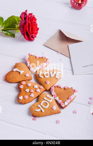 Des biscuits en forme de coeur avec je vous aime paroles comme cadeau pour amoureux le jour de la Saint-Valentin. Table en bois blanc avec carte de souhaits, de rose et de décor. Banque D'Images