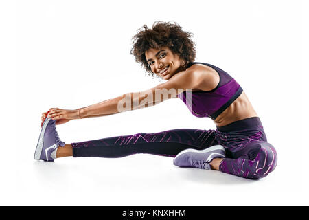 Fille sportive étend ses ischio-jambiers. Photo de smiling african girl doing exerçant sur fond blanc. Sports Banque D'Images