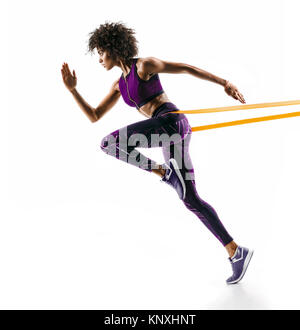 Strong girl en silhouette en utilisant une bande de résistance. Photo de jeune fille africaine effectue des exercices de conditionnement physique isolé sur fond blanc. Vue de côté Banque D'Images