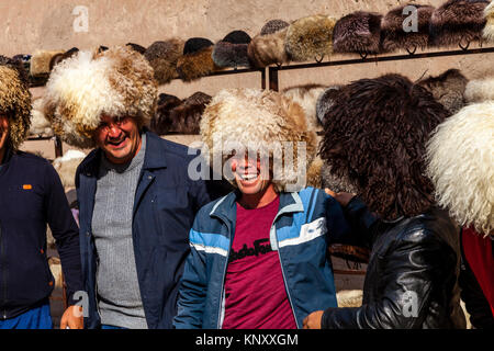 Un groupe de touristes ouzbeks rire alors qu'ils tentent sur les chapeaux de laine, Khiva, Ouzbékistan Banque D'Images