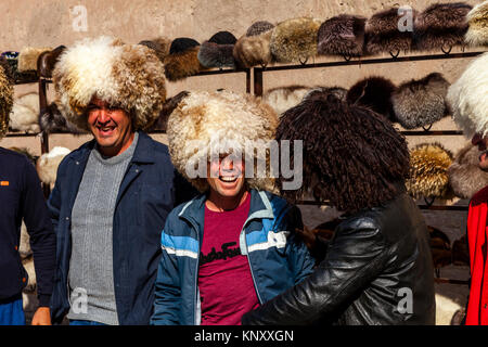 Un groupe de touristes ouzbeks rire alors qu'ils tentent sur les chapeaux de laine, Khiva, Ouzbékistan Banque D'Images