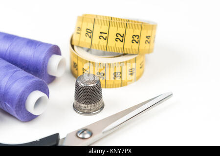 Outils et accessoires de couture, fils à coudre violet moyen, jaune ruban à mesurer avec des chiffres noirs, ciseaux et dé métal sur un fond blanc Banque D'Images