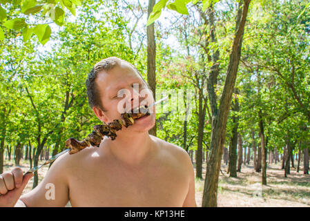 Homme mange shish kebab en brochettes, la nature dans la forêt Banque D'Images