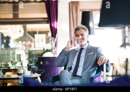 Mature businessman with smartphone dans un salon de l'hôtel. Banque D'Images