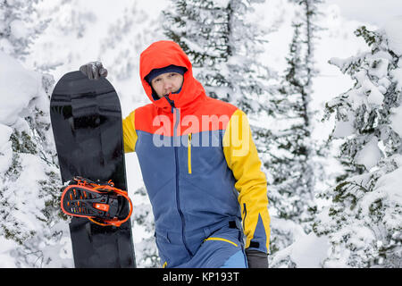 Freerider avec un snowboard dans des combinaisons se dresse au sommet d'une montagne enneigée. Banque D'Images