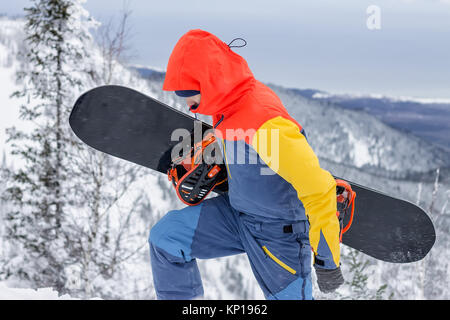 Freerider avec un snowboard dans des combinaisons se dresse au sommet d'une montagne enneigée. Banque D'Images