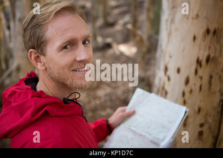 Portrait de jeune homme à la caméra en randonneur tout en maintenant une carte dans la forêt Banque D'Images